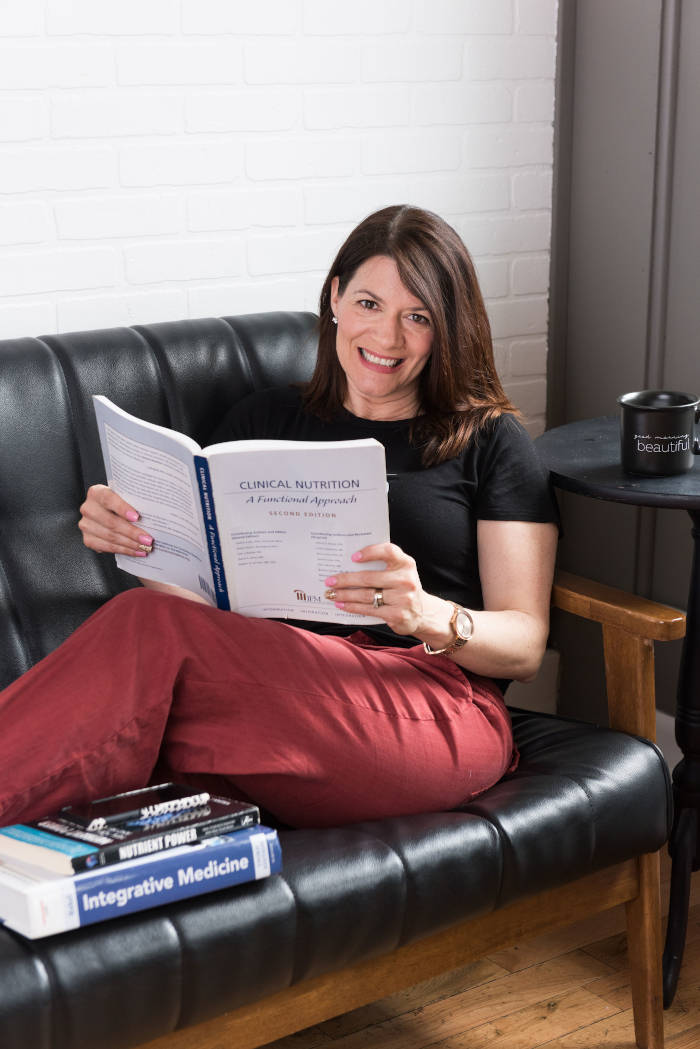 Amy Doyle sitting on couch reading functional nutrition books